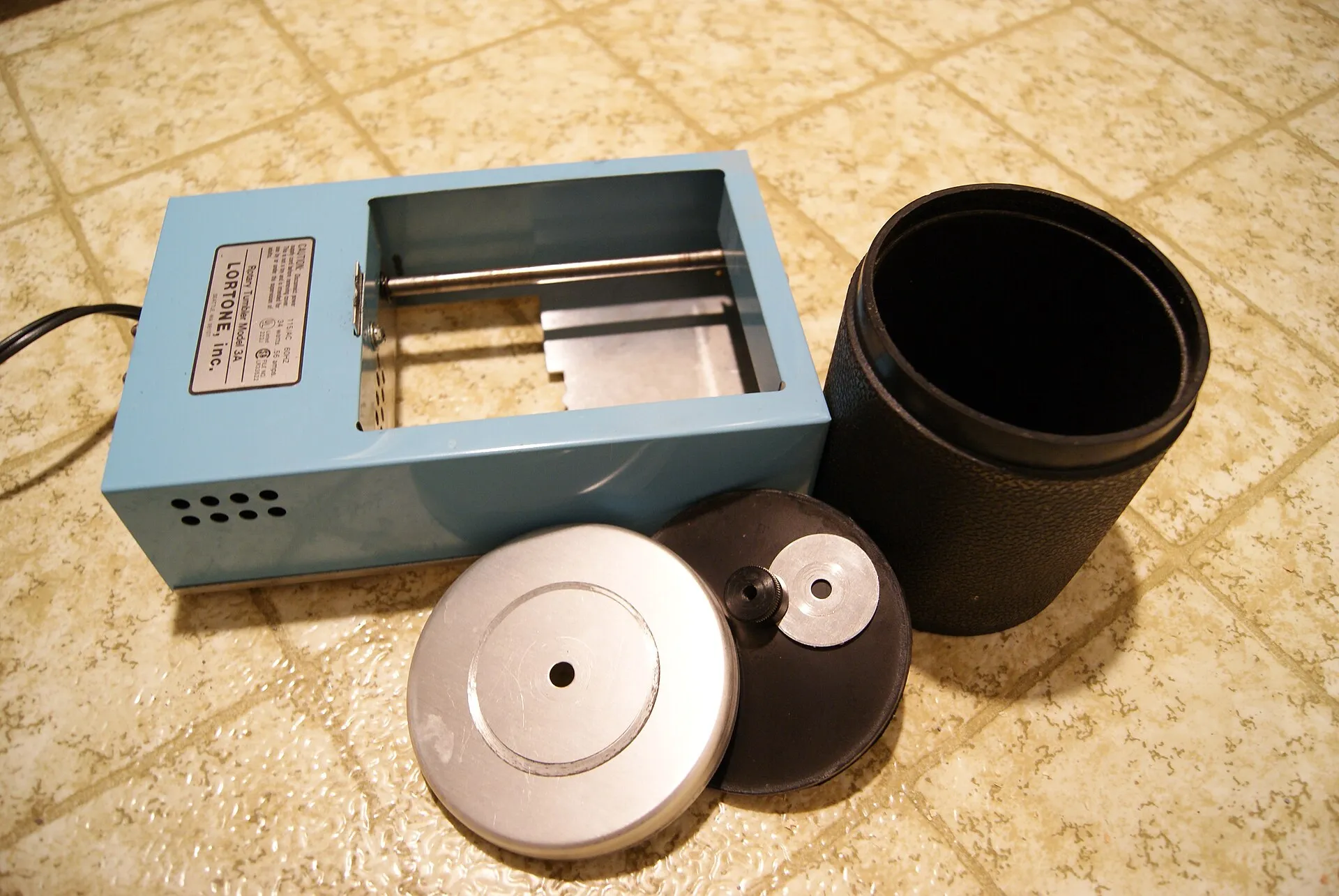 A small rotary rock tumbler with its rubber barrel and lid next to it